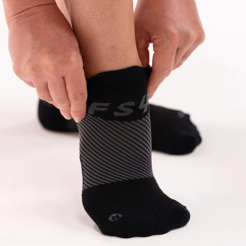 Lifestyle image of someone putting on a pair of black no show plantar fasciitis socks