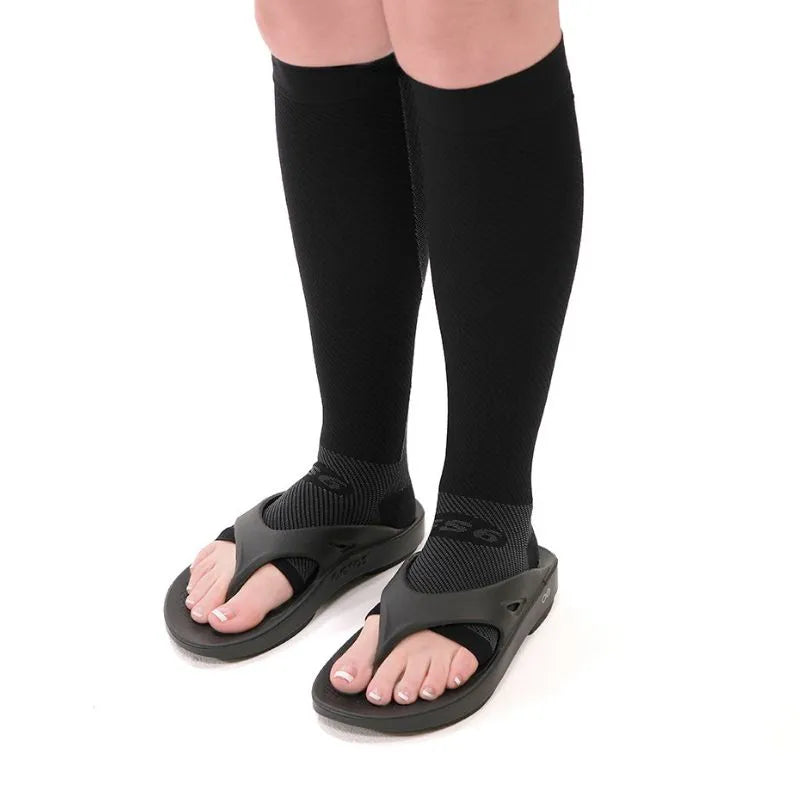 Lifestyle image of a person wearing the black compression leg sleeves with flip flops